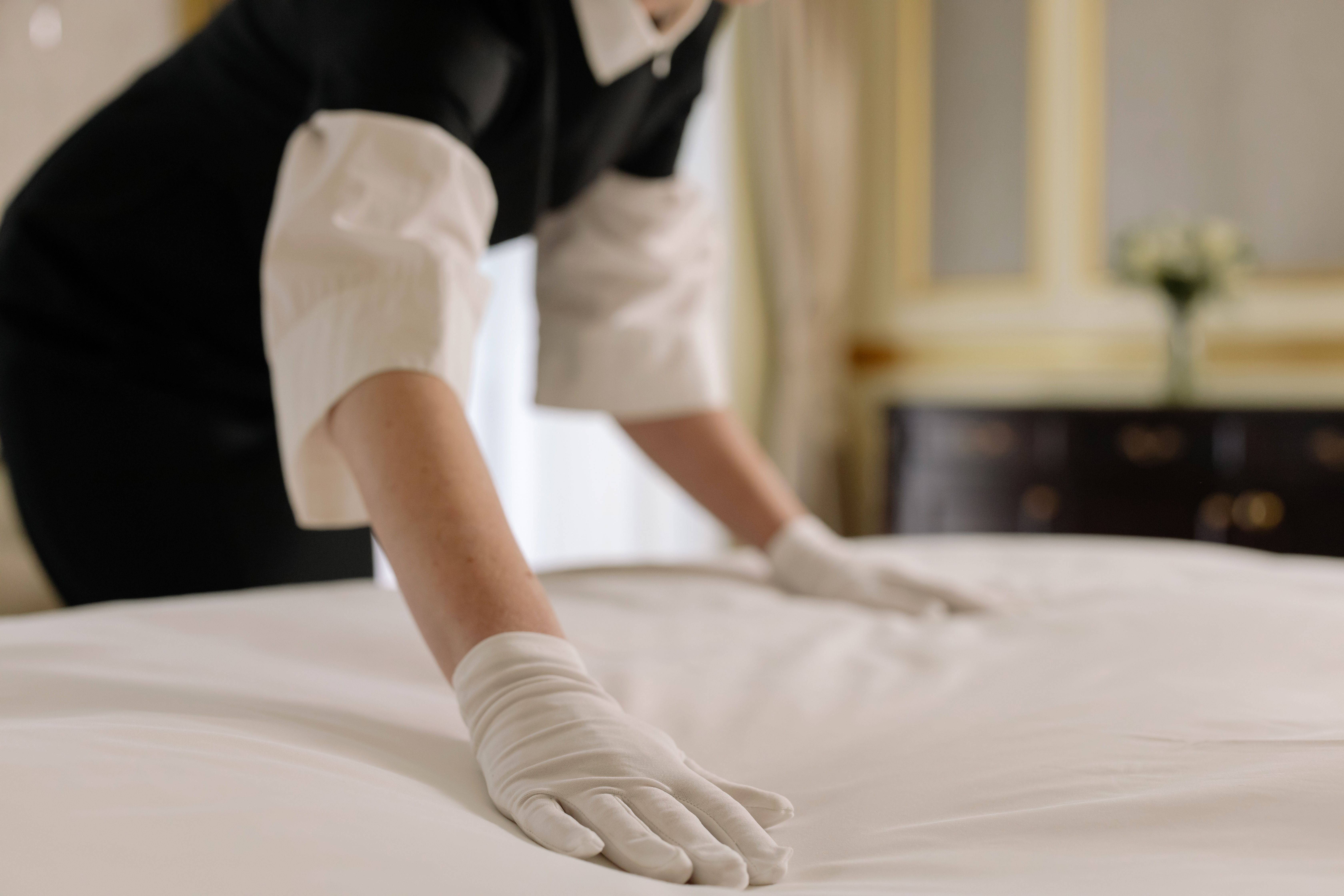 Housekeeper smoothing fresh white linens on a bed during a short-term rental turnover